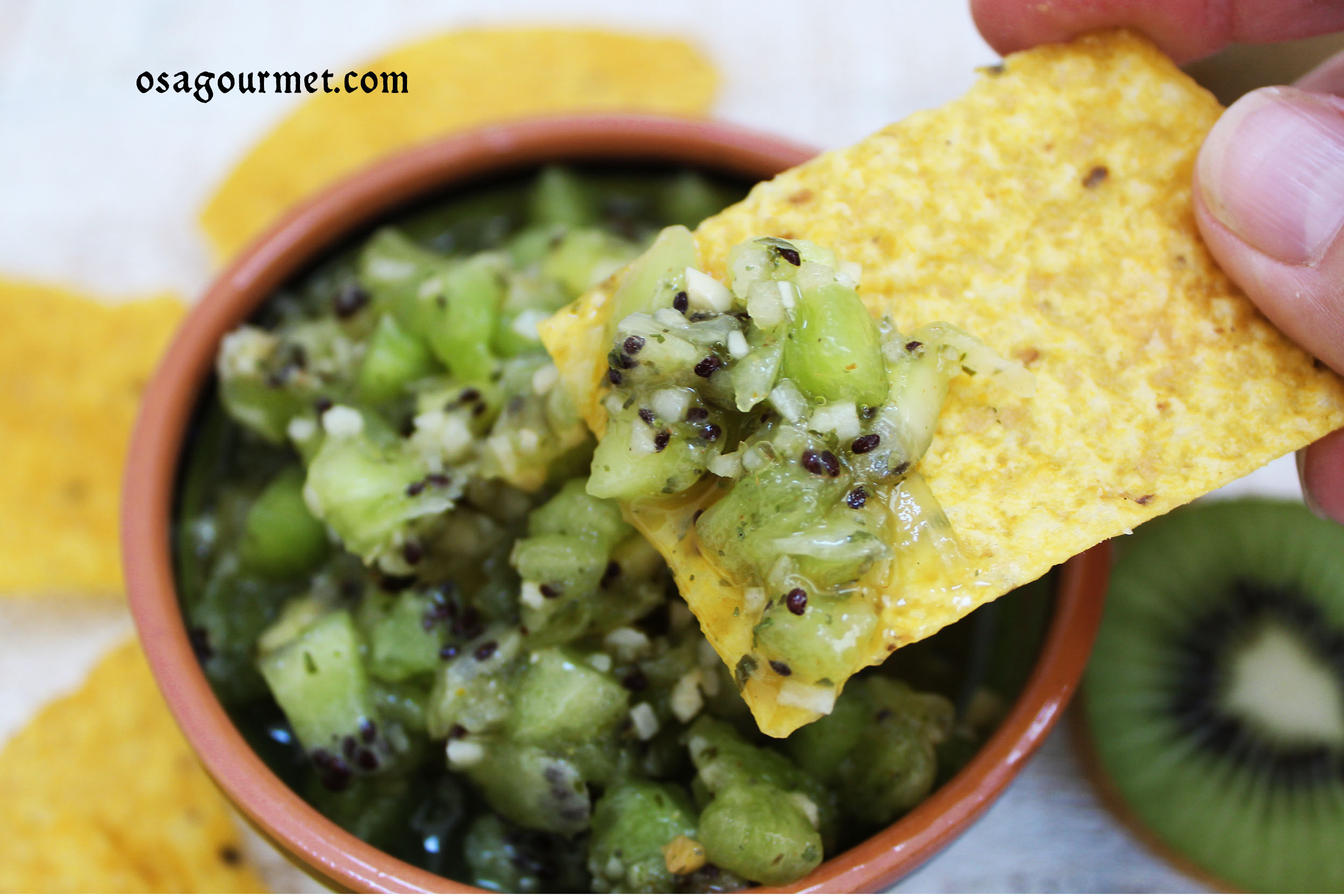kiwi salsa being dipped out of a bowl with a tortilla chip